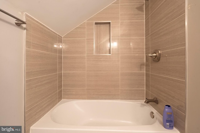 bathroom with tiled shower / bath combo and vaulted ceiling