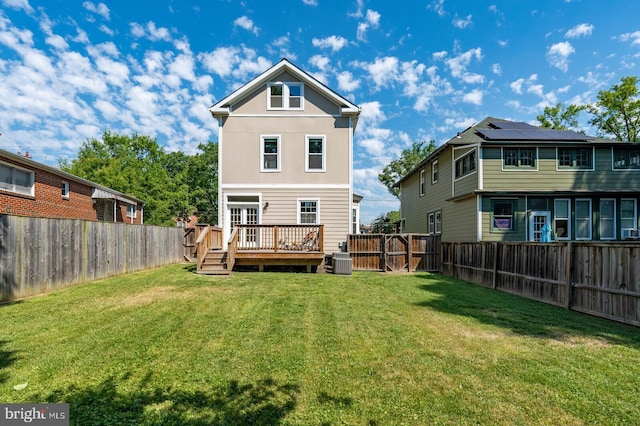 rear view of property with a lawn, a wooden deck, central air condition unit, and solar panels