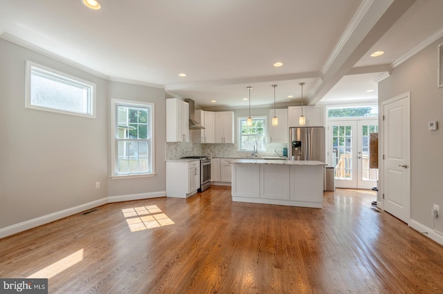 kitchen with a center island, french doors, wall chimney exhaust hood, appliances with stainless steel finishes, and decorative light fixtures