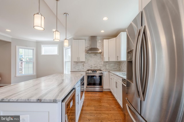 kitchen featuring backsplash, light stone counters, stainless steel appliances, wall chimney range hood, and white cabinetry