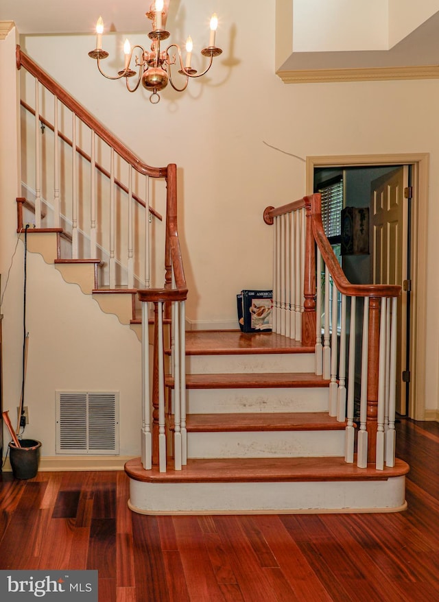 staircase with wood-type flooring, ornamental molding, and an inviting chandelier