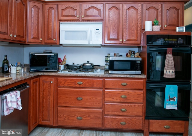 kitchen with light stone countertops, appliances with stainless steel finishes, and light hardwood / wood-style flooring