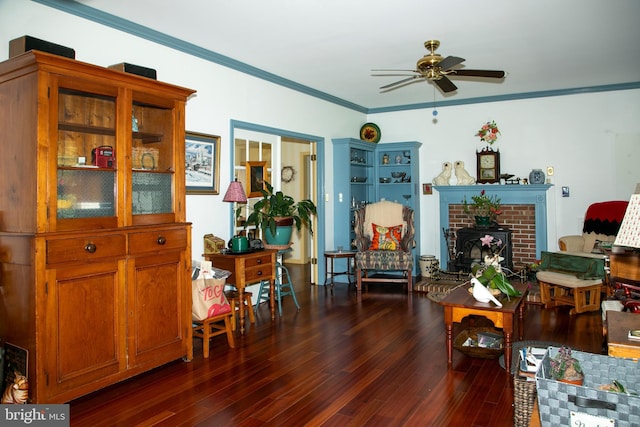 sitting room featuring ceiling fan, ornamental molding, dark wood-type flooring, and a brick fireplace