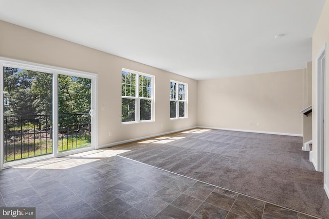 unfurnished living room featuring a healthy amount of sunlight and dark carpet