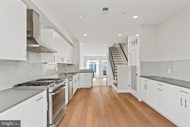 kitchen with white cabinetry, stainless steel appliances, wall chimney range hood, light hardwood / wood-style flooring, and sink