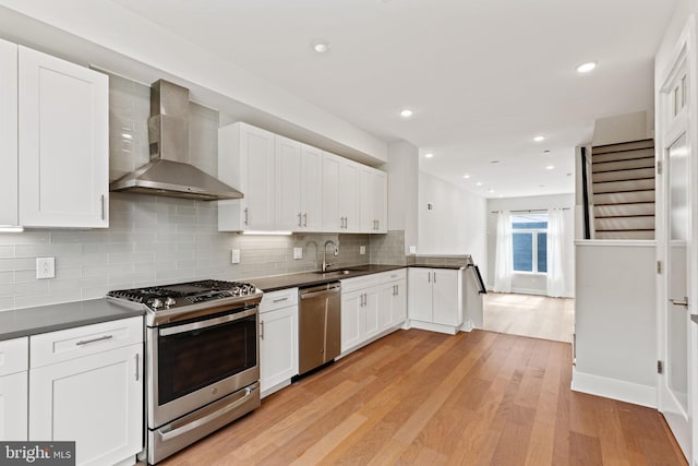 kitchen featuring stainless steel appliances, decorative backsplash, white cabinets, wall chimney range hood, and light hardwood / wood-style flooring