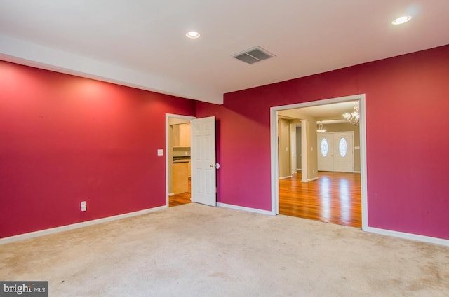 carpeted spare room featuring an inviting chandelier