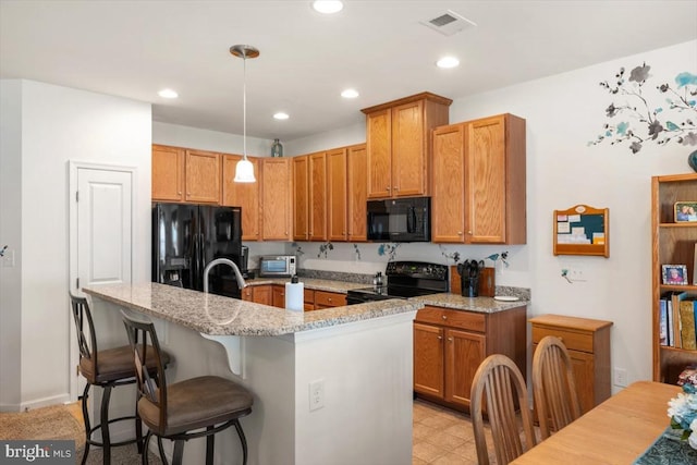 kitchen with light stone counters, a breakfast bar, black appliances, pendant lighting, and an island with sink