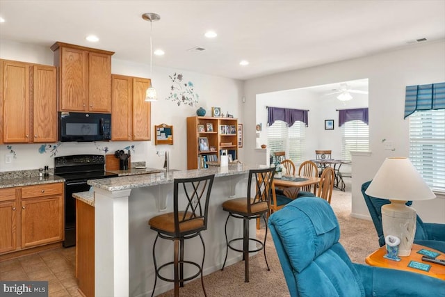 kitchen with a kitchen bar, light stone counters, black appliances, pendant lighting, and a center island with sink