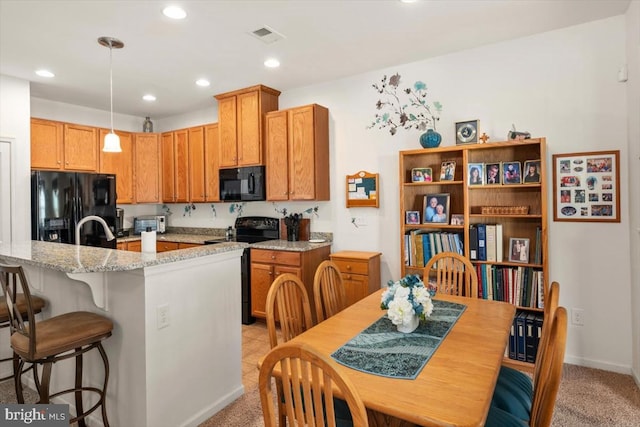 kitchen featuring pendant lighting, light carpet, black appliances, light stone countertops, and a breakfast bar area