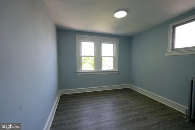 empty room with radiator heating unit and dark hardwood / wood-style flooring