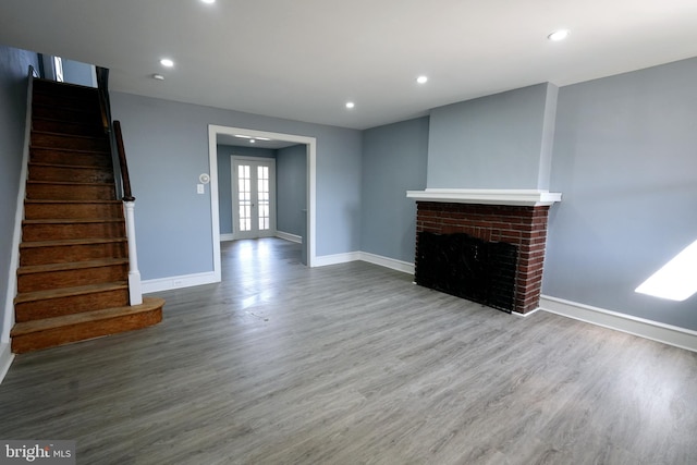 unfurnished living room featuring hardwood / wood-style flooring, french doors, and a brick fireplace