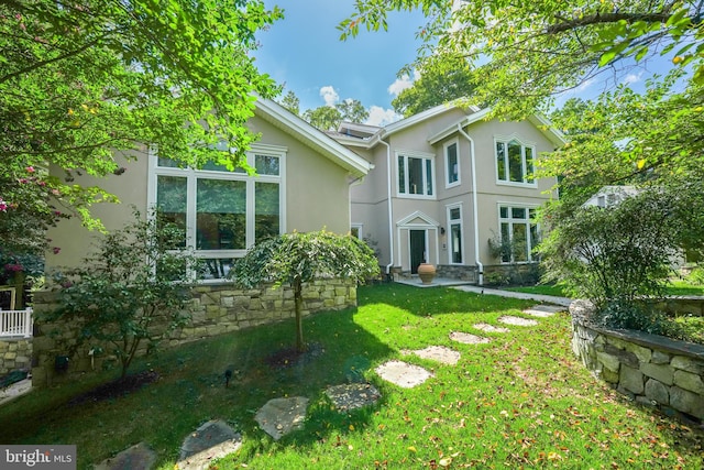 back of property with stone siding, a lawn, and stucco siding