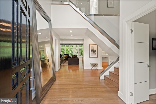 foyer with light wood finished floors, stairway, a high ceiling, and baseboards