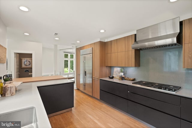 kitchen with stainless steel appliances, light countertops, brown cabinets, wall chimney exhaust hood, and modern cabinets