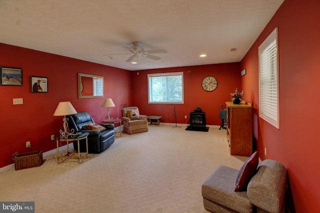 living area featuring a wood stove, ceiling fan, carpet floors, and a textured ceiling