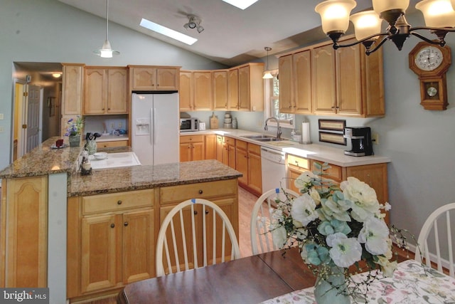 kitchen with vaulted ceiling with skylight, pendant lighting, white appliances, and sink