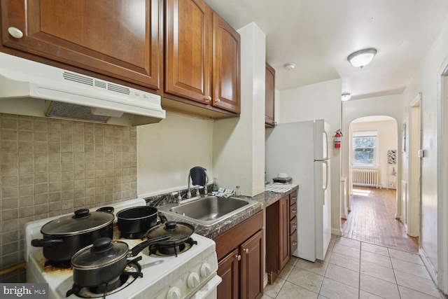 kitchen with white appliances, sink, decorative backsplash, light tile patterned floors, and radiator heating unit