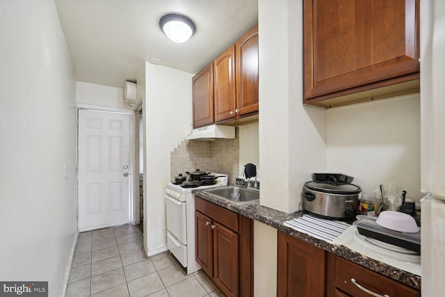 kitchen with white gas range, sink, dark stone countertops, decorative backsplash, and light tile patterned flooring