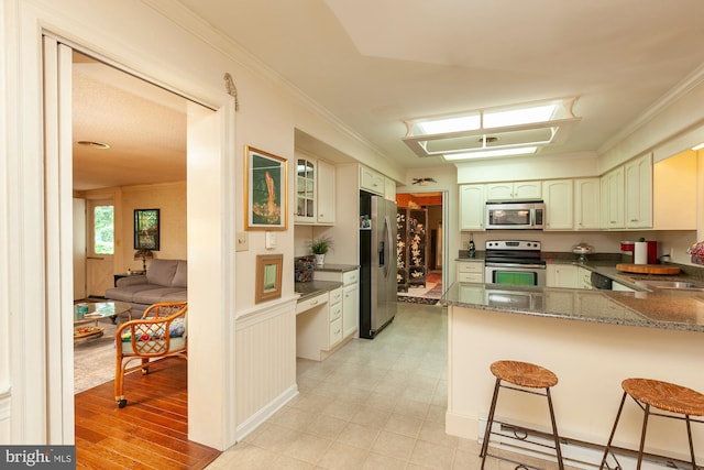 kitchen featuring a kitchen bar, dark stone countertops, ornamental molding, kitchen peninsula, and stainless steel appliances