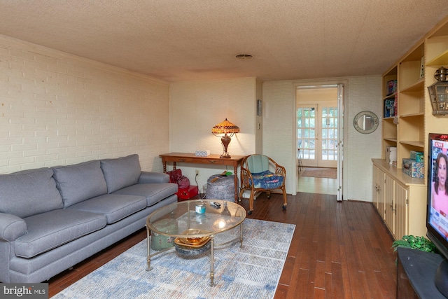 living room featuring dark wood-type flooring, a textured ceiling, and brick wall