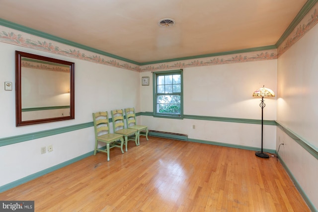 living area with crown molding, baseboard heating, and light wood-type flooring