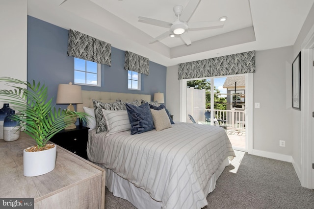 carpeted bedroom with access to exterior, baseboards, a tray ceiling, and a ceiling fan