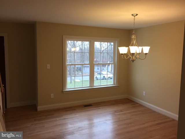 unfurnished dining area with a notable chandelier, wood finished floors, visible vents, and baseboards