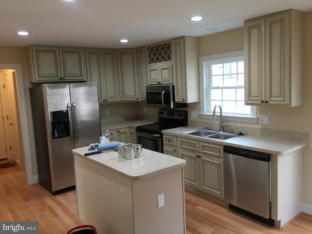 kitchen with a sink, a kitchen island, light countertops, appliances with stainless steel finishes, and light wood finished floors