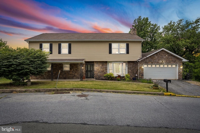 traditional-style home with a chimney, a lawn, driveway, stone siding, and a garage