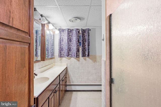 bathroom with a baseboard heating unit, a paneled ceiling, tile walls, tile patterned flooring, and vanity