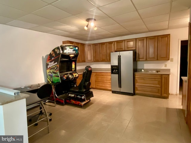 kitchen featuring brown cabinets, a drop ceiling, light tile patterned floors, stainless steel fridge with ice dispenser, and light countertops