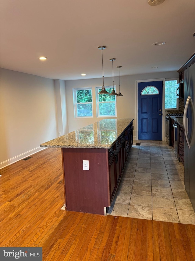 kitchen with light stone countertops, appliances with stainless steel finishes, light wood-type flooring, a center island, and hanging light fixtures