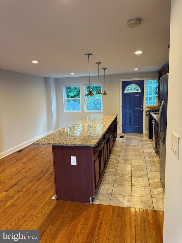 kitchen with pendant lighting, black refrigerator, light hardwood / wood-style flooring, light stone countertops, and a kitchen island