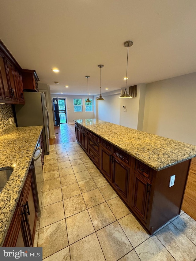 kitchen with pendant lighting, light stone counters, tasteful backsplash, and a center island