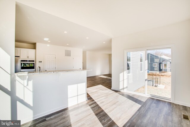 2107 Warrenton Rd, Fredericksburg, VA 22406 - kitchen featuring stainless steel oven, dark wood-style floors, white cabinetry, a breakfast bar area, and light stone countertops