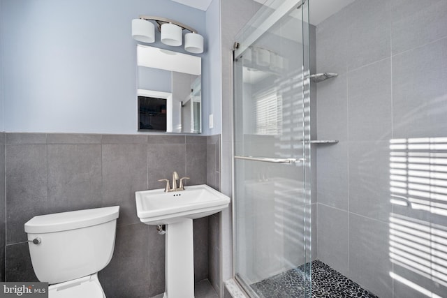 bathroom featuring sink, toilet, a shower with shower door, and tile walls