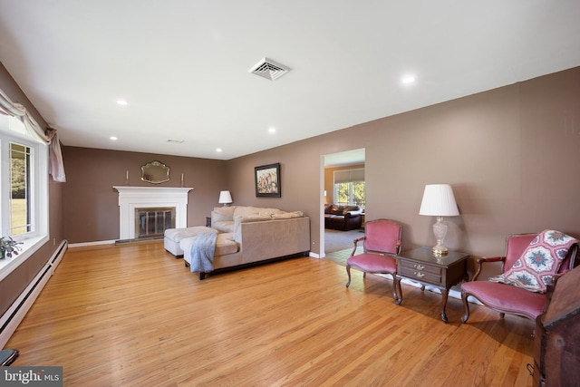 living room featuring baseboard heating, a healthy amount of sunlight, and light wood-type flooring