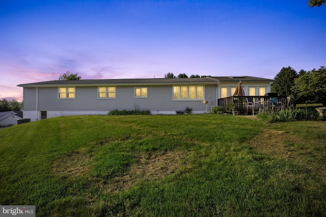 back house at dusk with a lawn and a deck