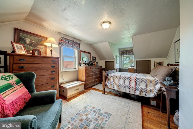 bedroom with a textured ceiling, light hardwood / wood-style flooring, and vaulted ceiling