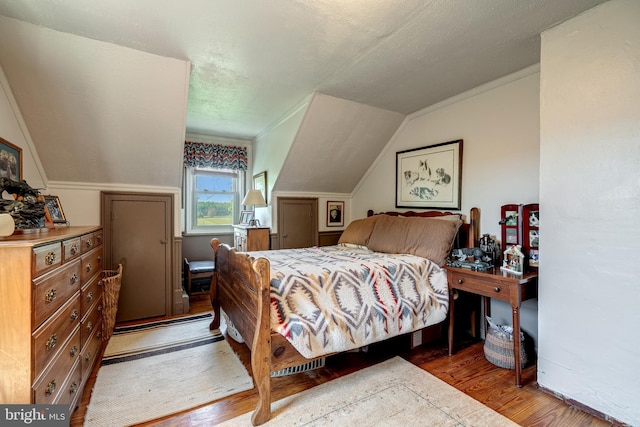 bedroom featuring a textured ceiling, ornamental molding, vaulted ceiling, and hardwood / wood-style flooring