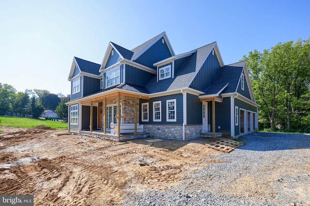 view of front of home featuring driveway, a shingled roof, stone siding, a standing seam roof, and board and batten siding