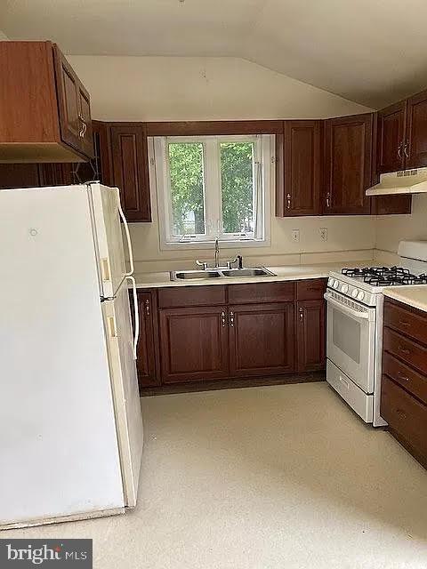 kitchen featuring white appliances, vaulted ceiling, and sink