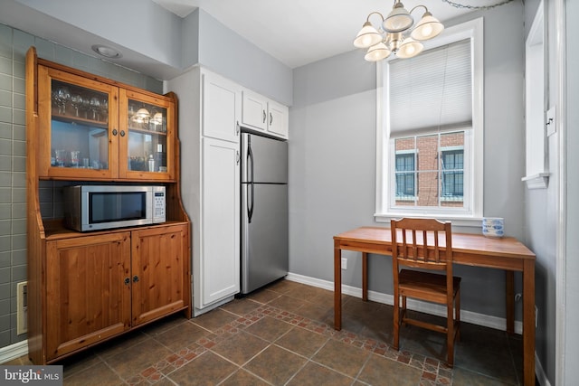 kitchen with stainless steel appliances, dark tile patterned floors, an inviting chandelier, tile walls, and white cabinetry