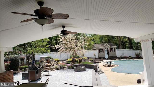 view of patio featuring ceiling fan, a shed, a covered pool, and an outdoor fire pit