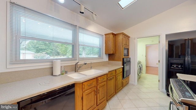 kitchen with vaulted ceiling with skylight, black appliances, sink, rail lighting, and light tile patterned flooring