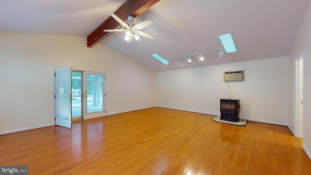 unfurnished living room featuring lofted ceiling with skylight, a wood stove, light hardwood / wood-style flooring, an AC wall unit, and ceiling fan