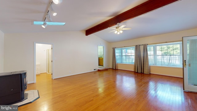 unfurnished living room with light wood-type flooring, a wood stove, track lighting, vaulted ceiling with skylight, and ceiling fan