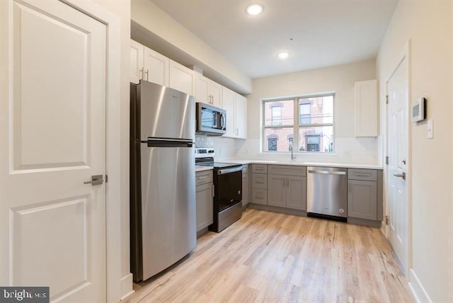 kitchen featuring gray cabinetry, sink, light wood-type flooring, white cabinetry, and stainless steel appliances