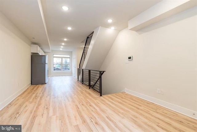 basement with stainless steel fridge and light hardwood / wood-style flooring